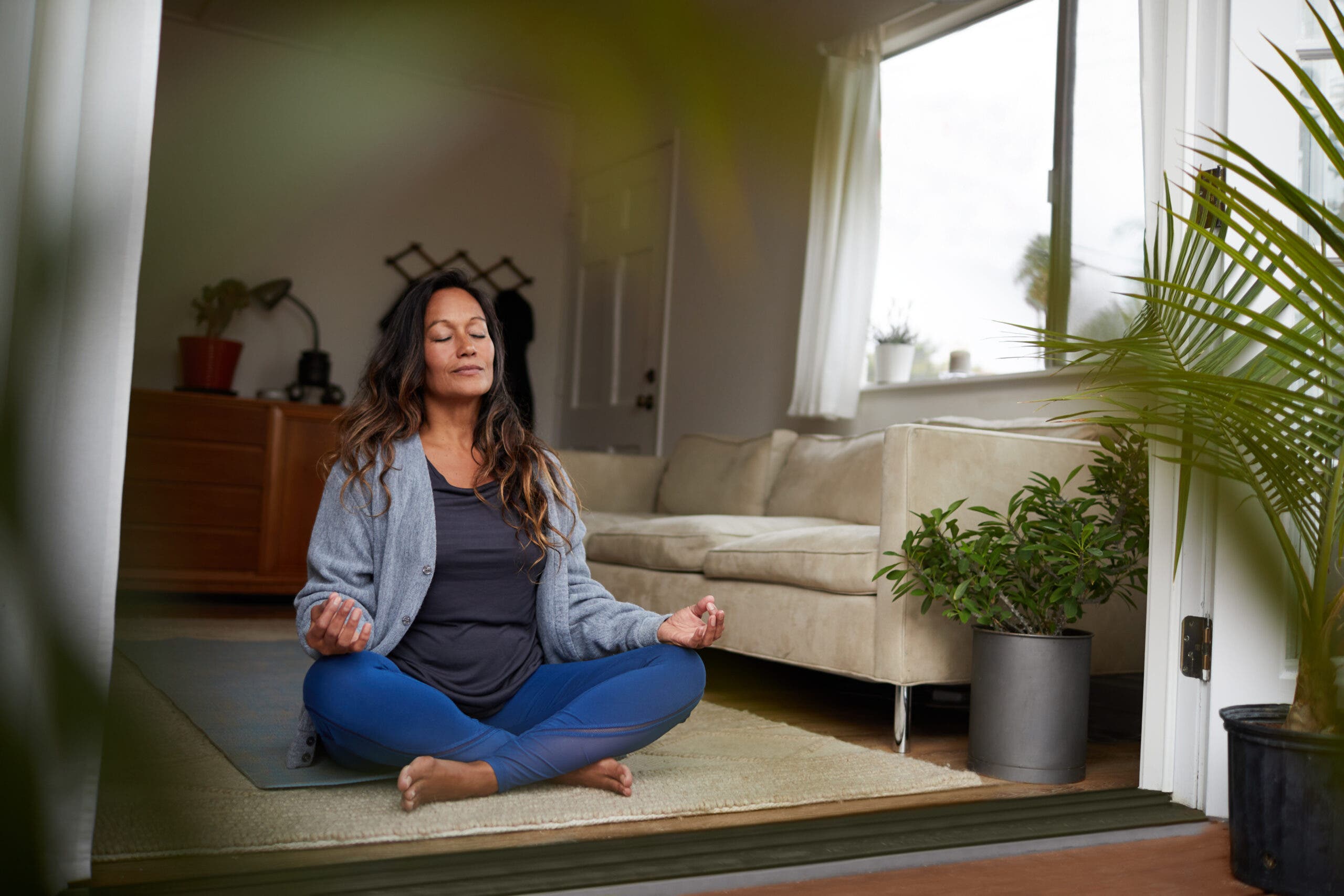Serene mature woman meditating with her eyes closed while practicing yoga on the floor of her living room at home