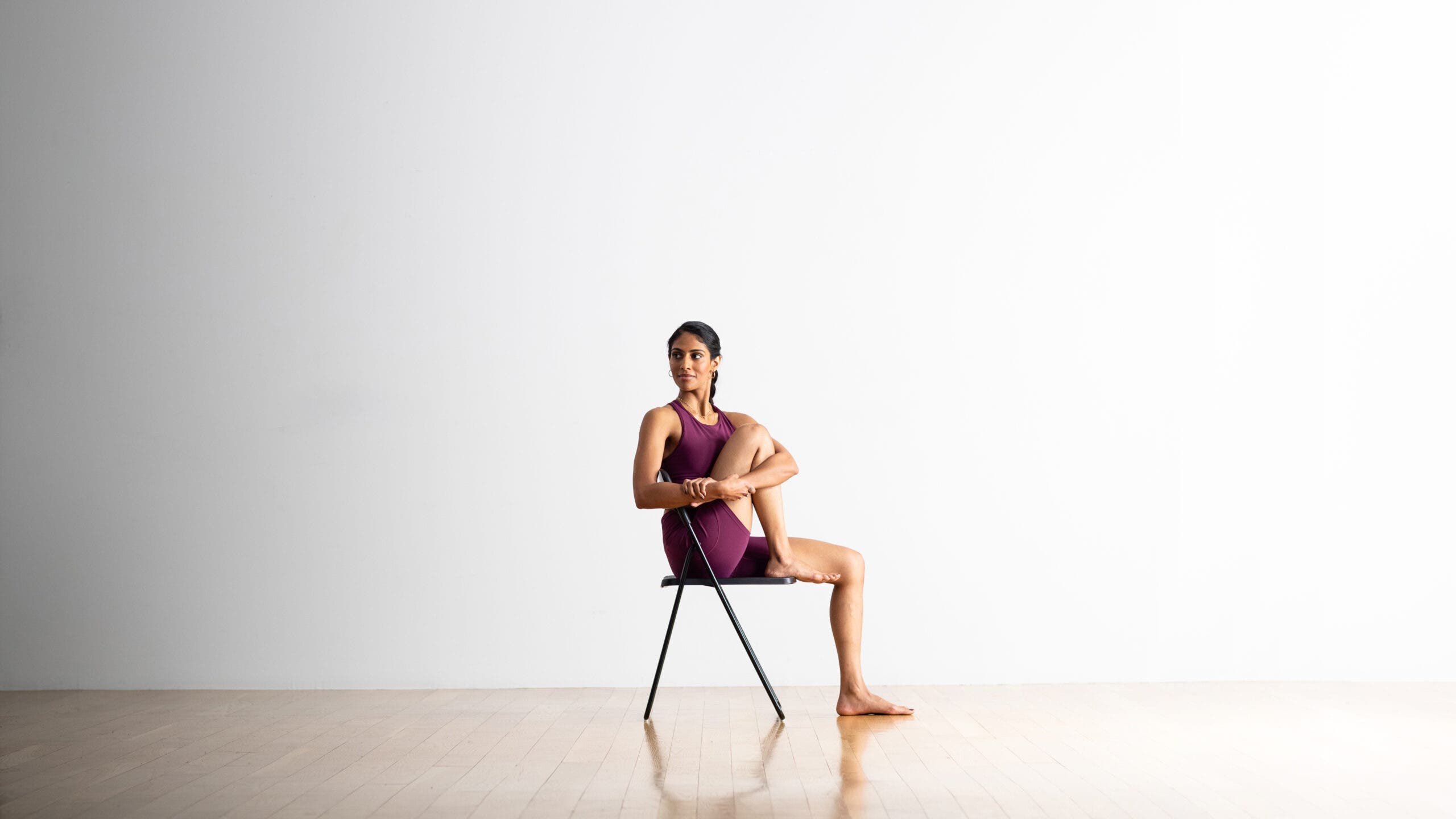 Neeti Narula practices Pasasana, Rope Pose, in a chair. She has one knee up and twists to the side.