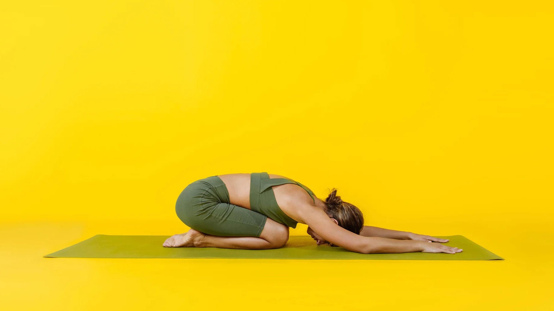 A person rests in Child's Pose in a yellow room