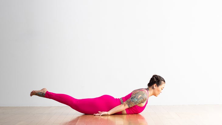 A person demonstrates a variation of Locust Pose in yoga, with their hands by their sides