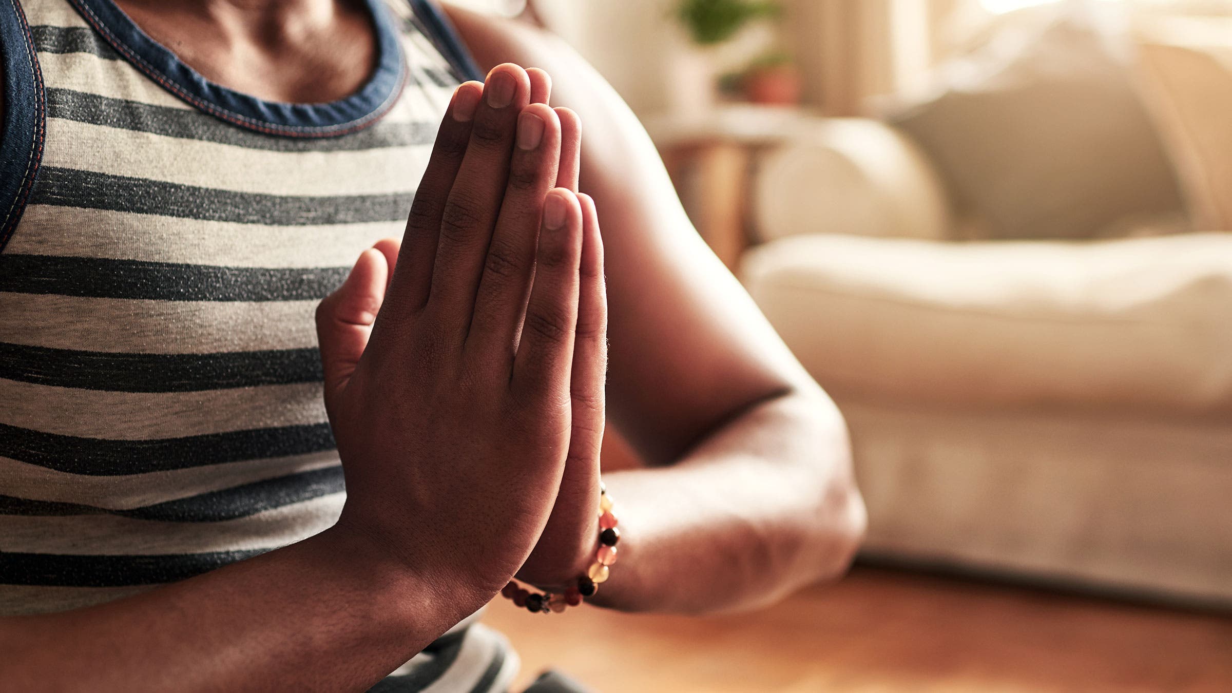 A man sits in meditation posture with his hands in Anjali Mudra (prayer hands)