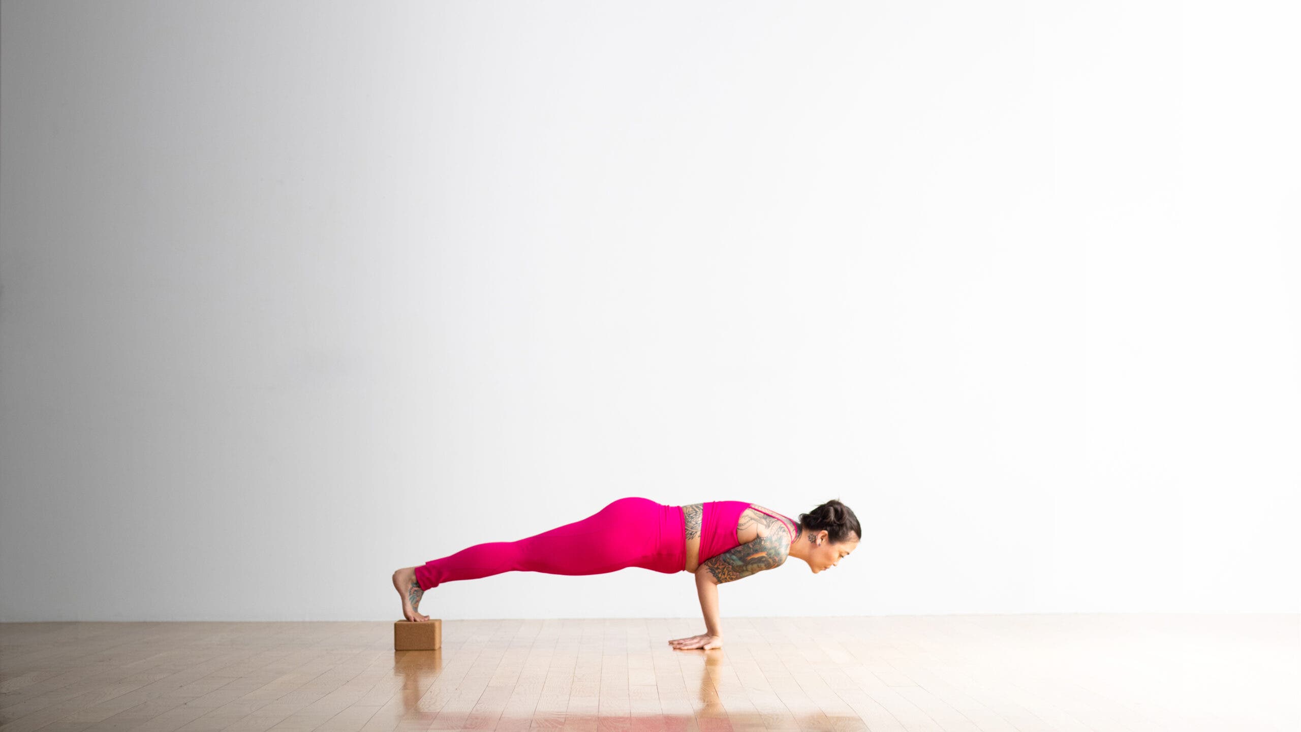 Woman in magenta yoga tights practices Peacock Pose with her feet on blocks.