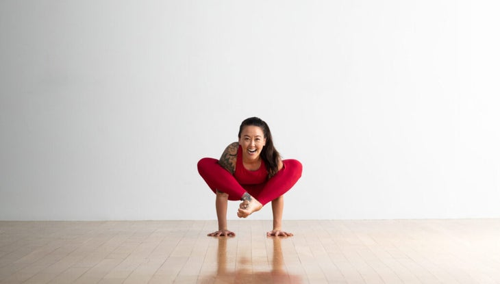 Soozie Kinstler presses up into shoulder pressing pose. From a wide-legged seated position, she wraps her legs around her arms and lifts up into Shoulder Pressing Pose