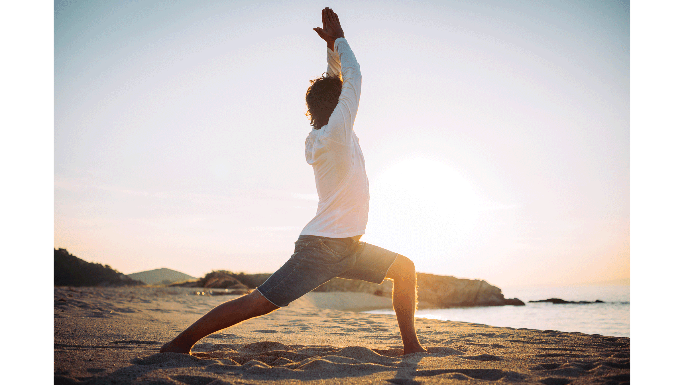 Man on the beach at sunrise practicing yoga in Warrior 1 Pose