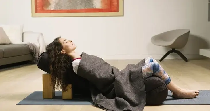 A woman lying on her back atop a bolster on her yoga mat.