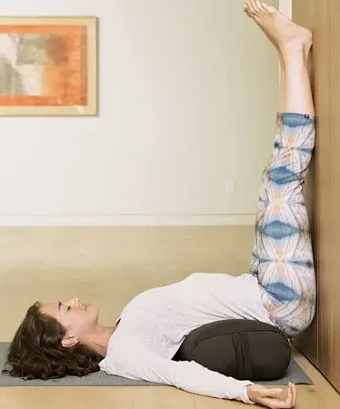 A woman performing Legs Up the Wall Pose on her yoga mat.