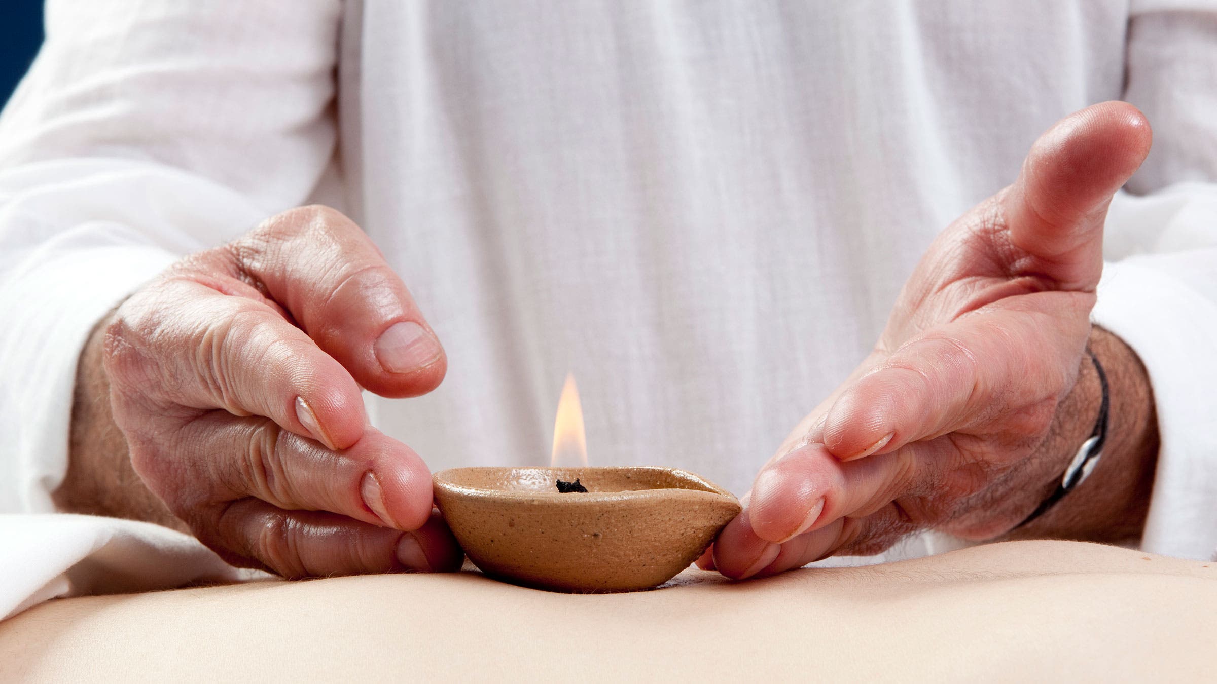 A pair of hands places a lit candle on the stomach of an individual for a chakra healing