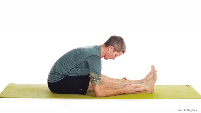 A man performs Paschimottanasana (Seated Forward Bend) in yoga