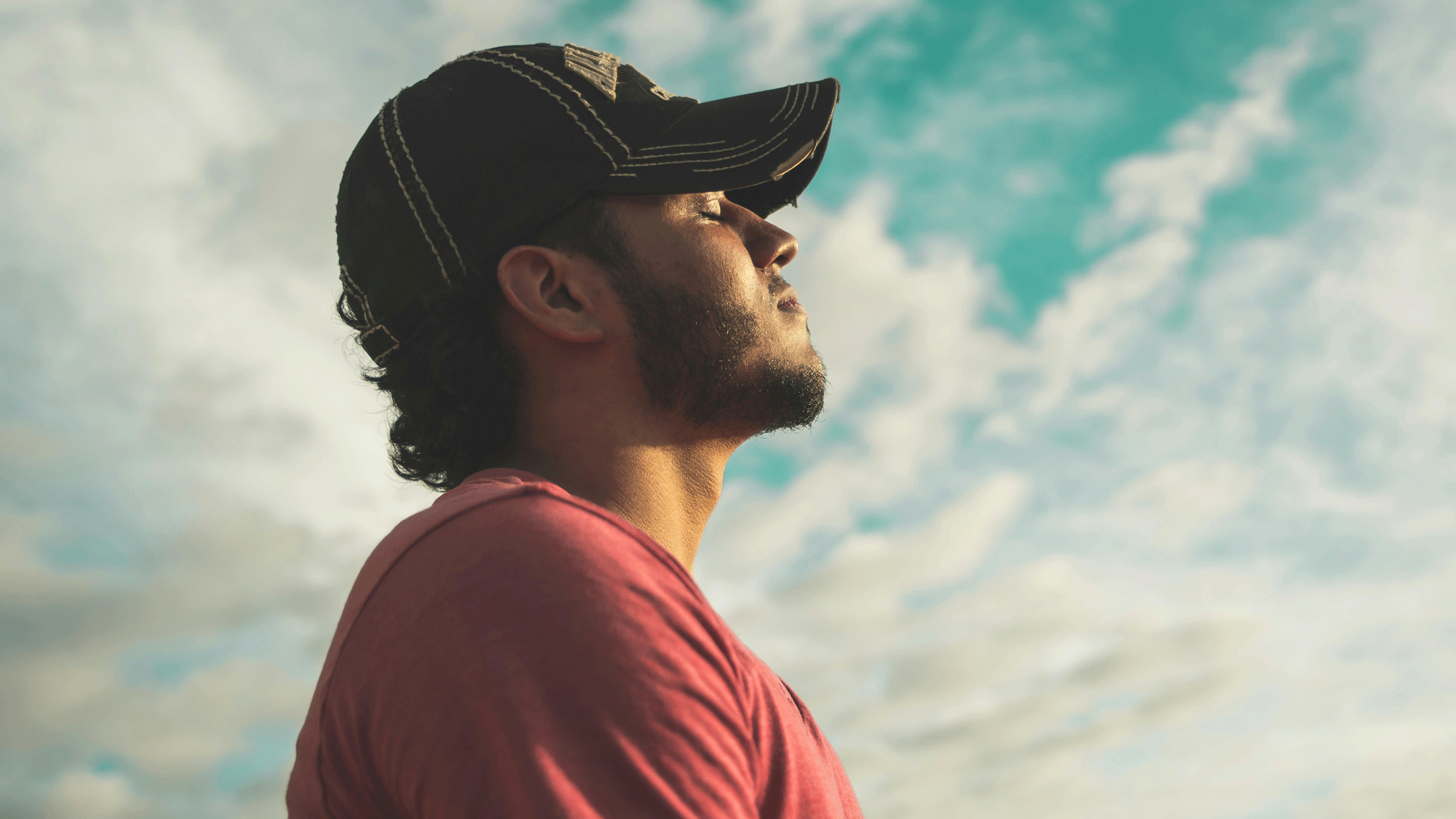 Young guy in a baseball cap sitting outside with his eyes closed practicing meditation posture
