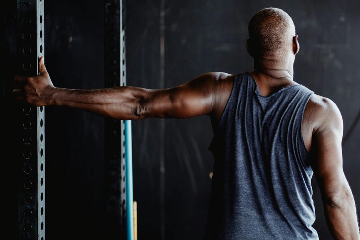 Man holding onto a metal bar in a gym, stretching his chest.