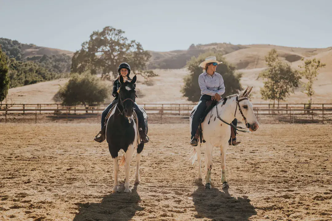 View of adult and child riding horses on dude ranch.