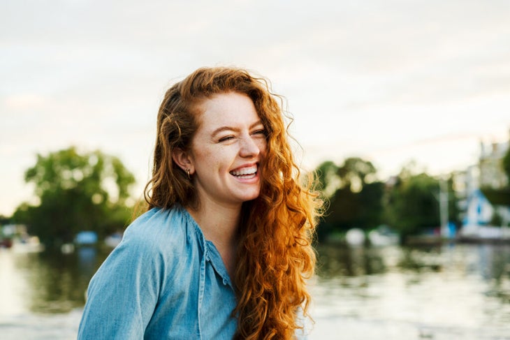 Young woman smiling outside next to a lake.