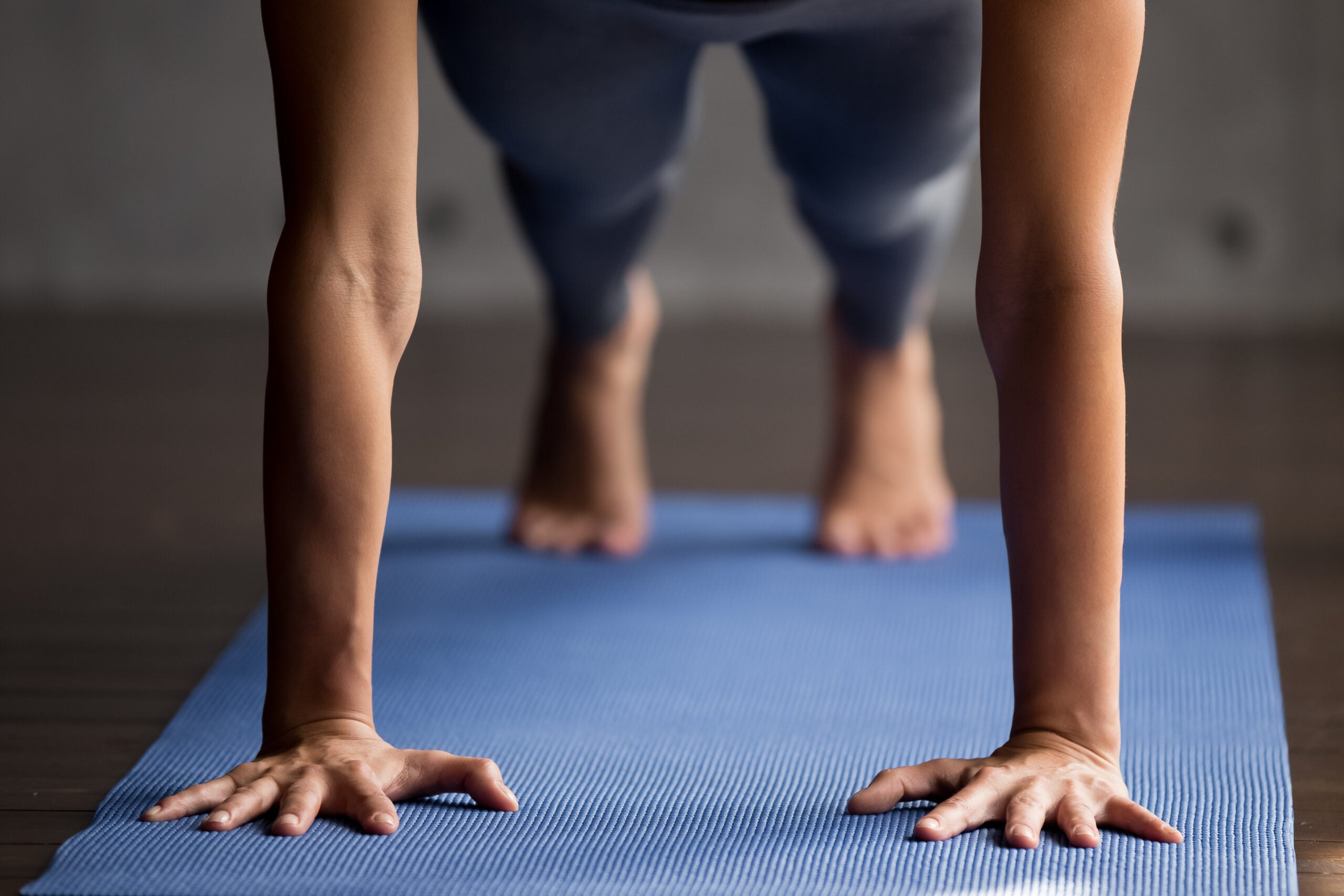 Close up of woman's hands and feet in plank position on a blue yoga mat.