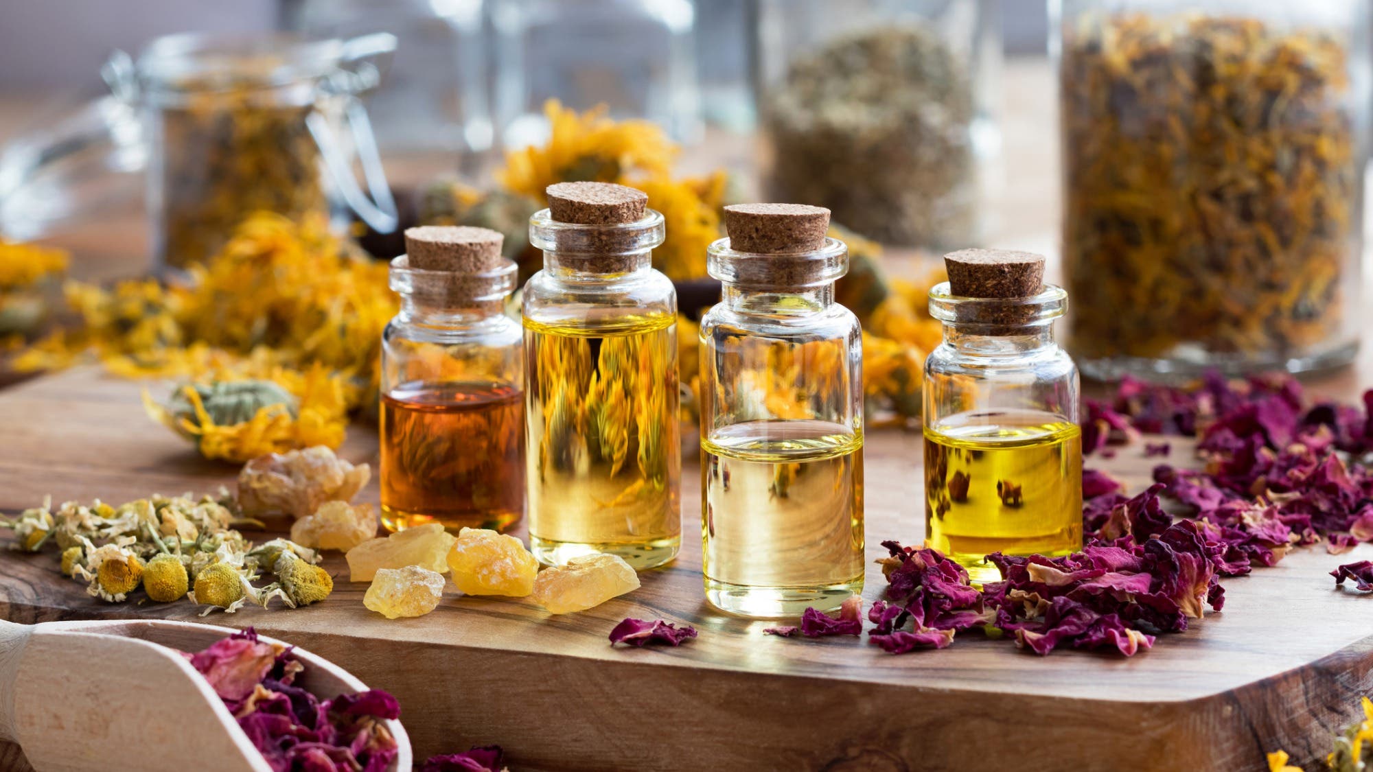 Bottles of essential oils are shown with dried rose petals, chamomile, calendula.