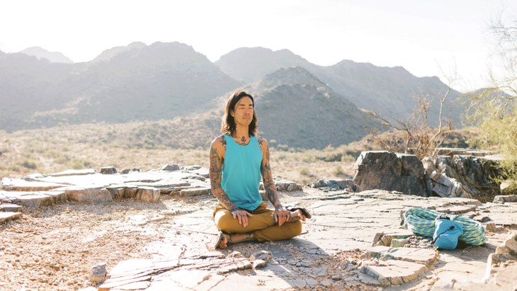 Man outside on a rocky ledge amount mountains practiicng yoga for climbers.