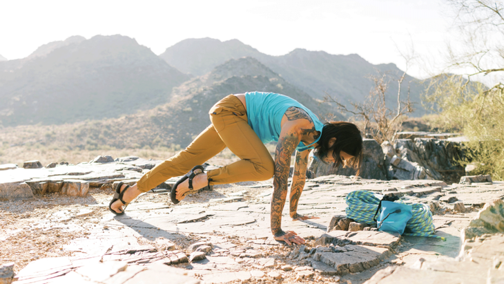 Man practicing a type of yoga crunch from Downward Facing Dog as he practices yoga for climbers on a rocky outcropping in the desert
