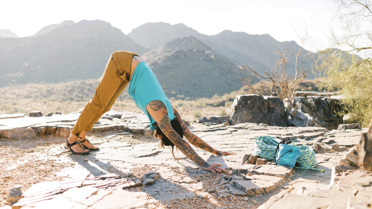 Man practicing Downward-Facing Dog during a yoga for climbers session on a rocky outcropping with the morning sun in the background