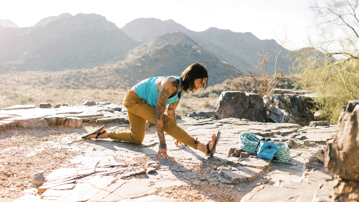 Man practicing half splits on a rocky outcropping in the desert with his right leg extended straight ahead and his back knee on the ground.