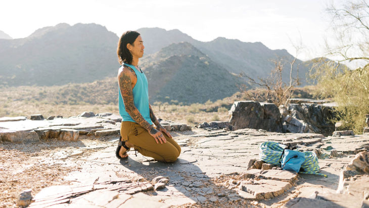 A rock climber kneeling back with his toes tucked under for a stretch along the bottom of the feet.