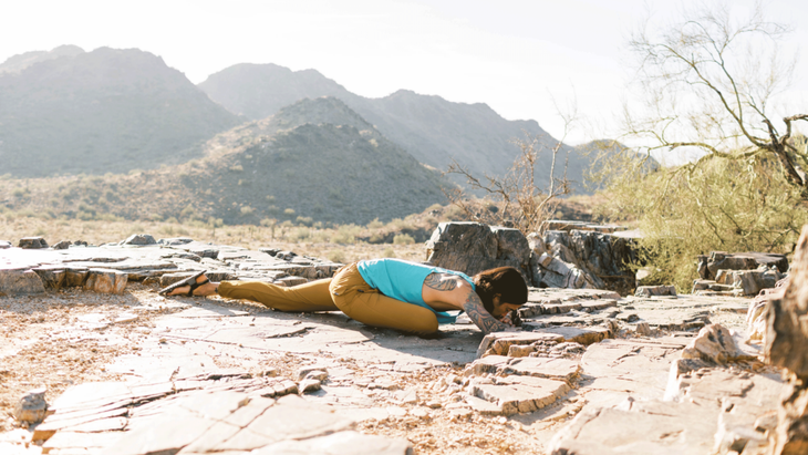 Man practicing yoga for climbers on a rocky ledge among mountains.