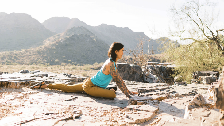 Man practicing yoga for climbers on a rocky outcropping with his left leg behind him and his right knee bent in front of him.