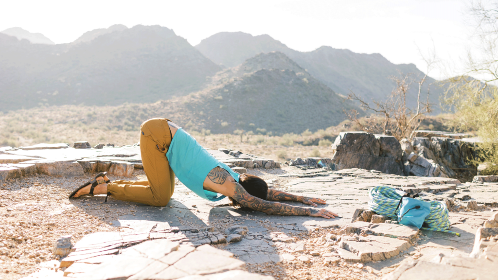 Man on hands and knees on a rocky ledge practicing Puppy Pose as part of a yoga for climbers sequence before rock climbing.