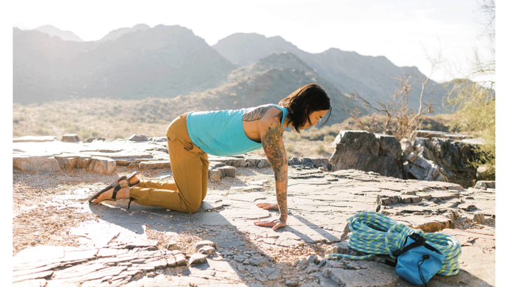 Man kneeling on a rock doing yoga for climbers with his hands beneath his shoulders and his hips above his knees.