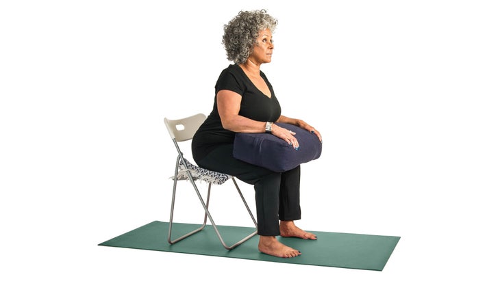 Woman using a bolster to assist with cobra pose in a chair