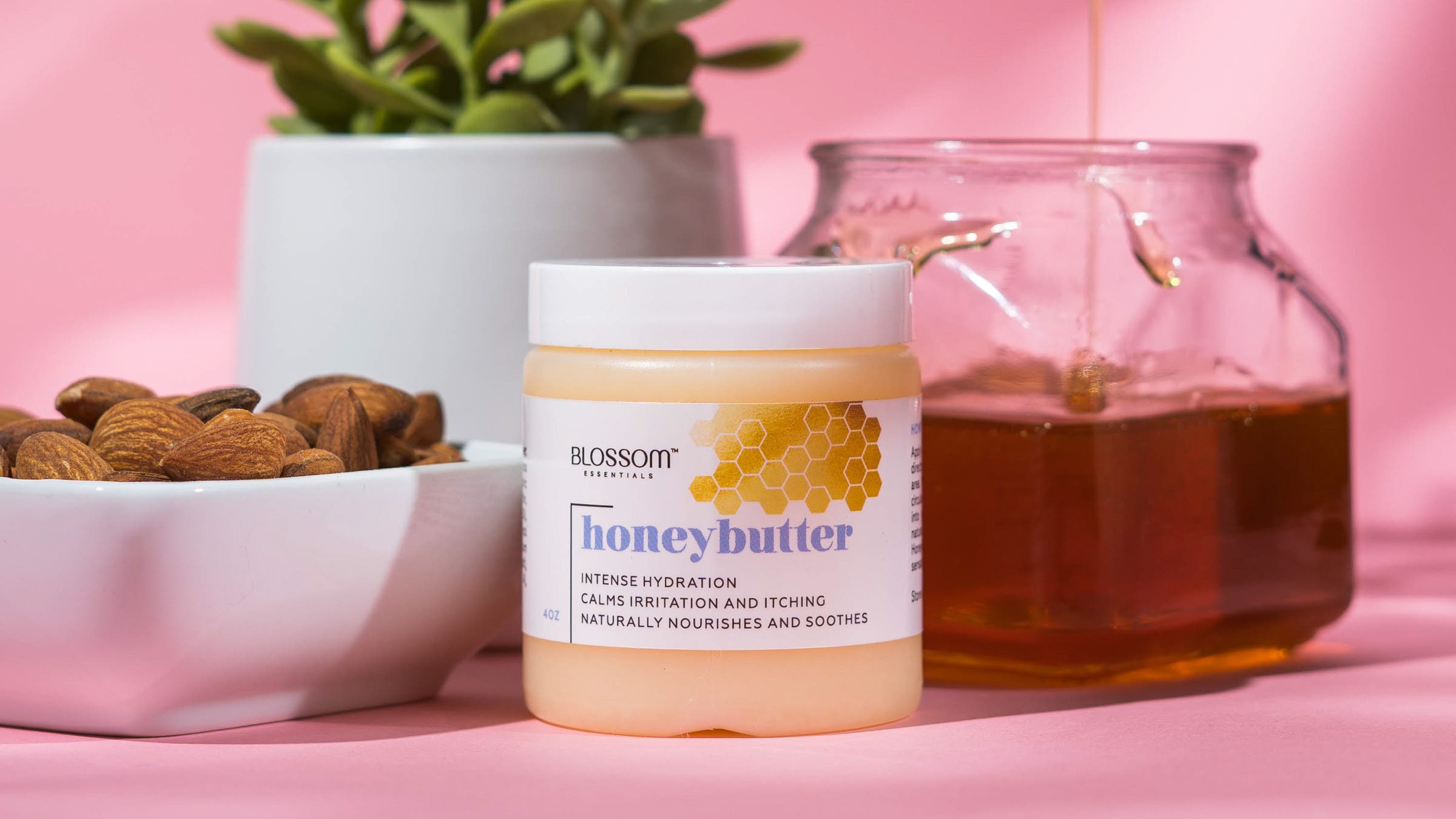 Blossom honey butter next to bowl of almonds and container of honey on pink background