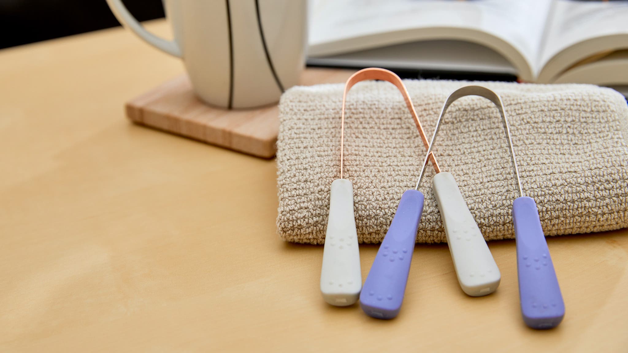 Copper and Stainless Steel tongue cleaner on table with book and cup