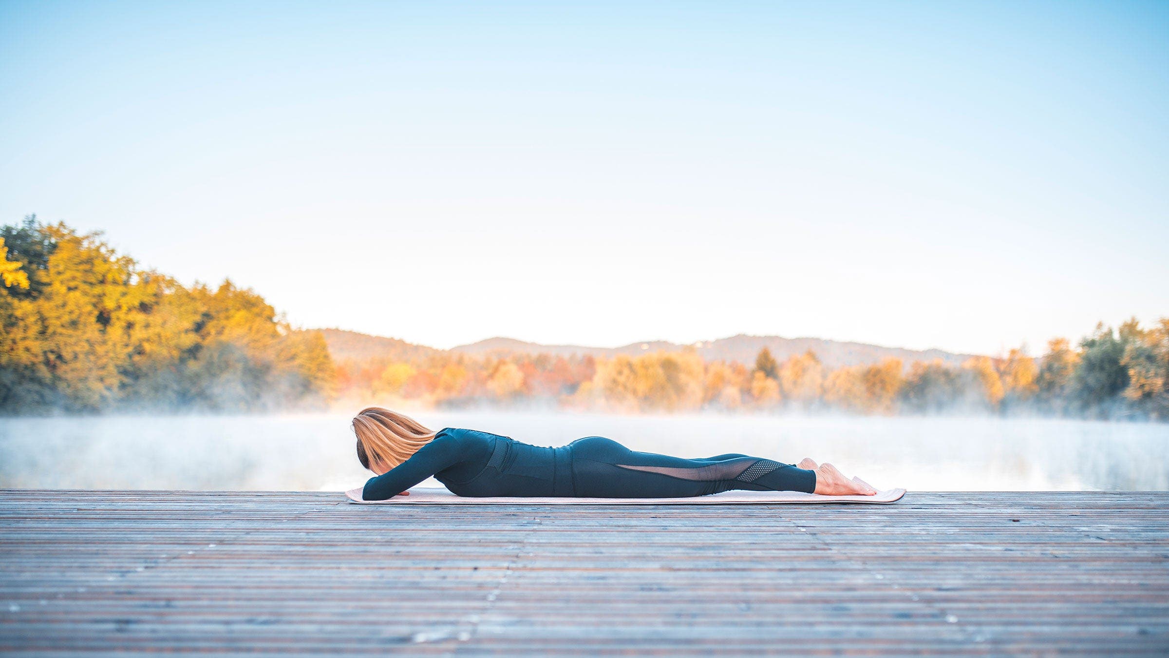 A woman demonstrates crocodile pose while lying on a deck with mountains