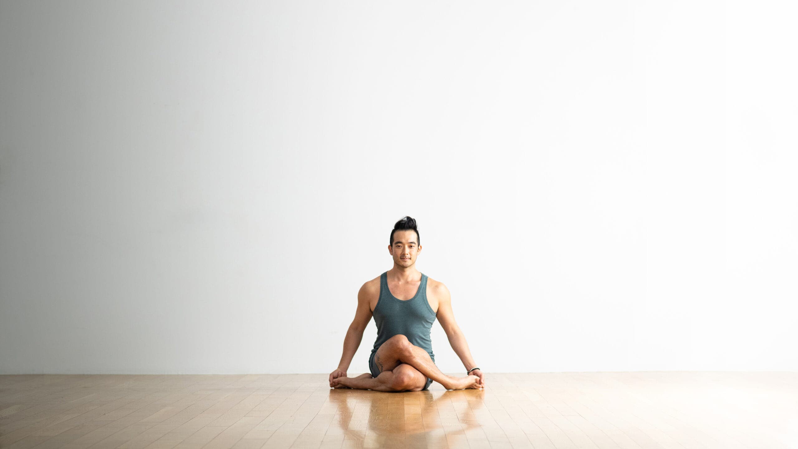 Hiro Landazuri sits with his legs crossed in Gomukhasana variation, Cow Face Pose