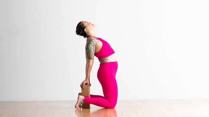 Woman performing a Camel Pose modification with a block