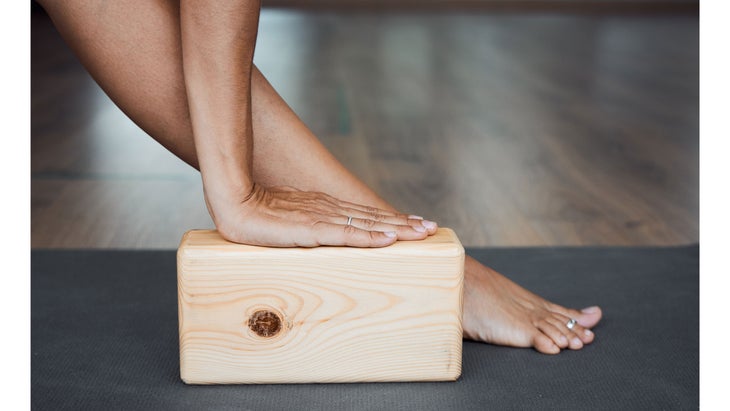 A person practices yoga with one hand on a yoga block next to their foot.