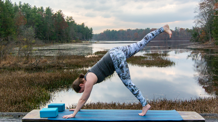 Anna Engels in 3-legged downward facing dog pose against a backdrop of stream and woods