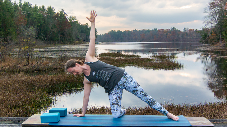 Anna Engels inAnna Engels in kneeling side plank against a backdrop of stream and woods