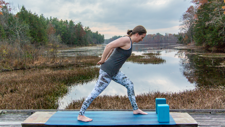 Anna Engels in Humble Warrior variation against a backdrop of stream and woods