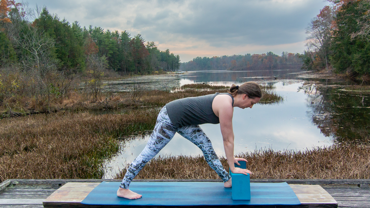 Anna Engels in Pyramid pose with straight legs against a backdrop of stream and woods