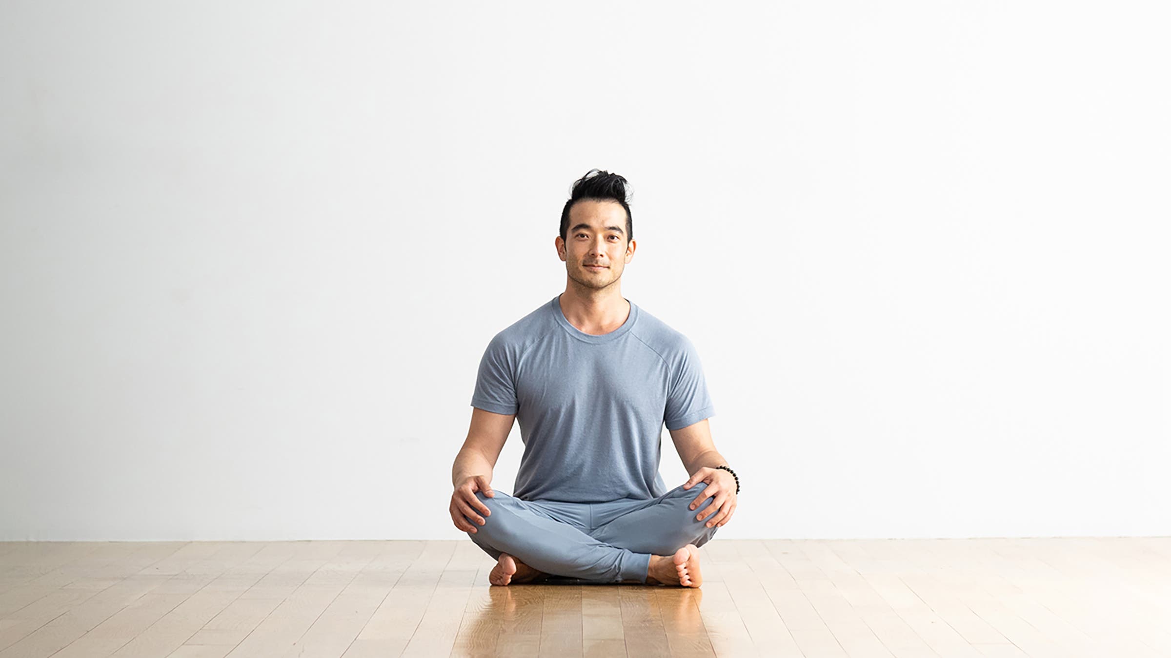 Man sitting cross-legged on a hardwood floor in the pose known as Easy Seat (Sukhasana)