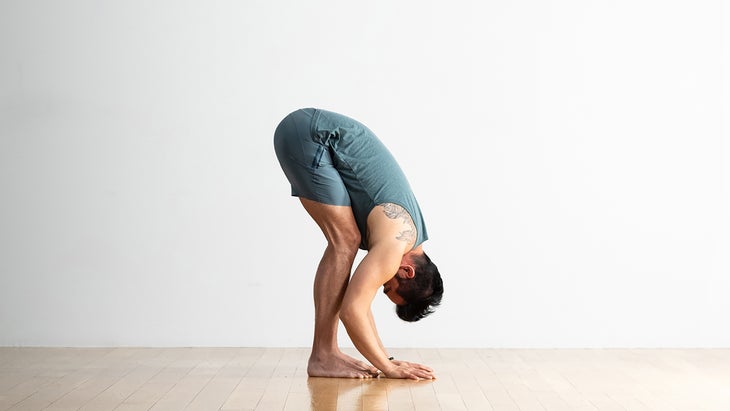 A person stands with his knees bent and does a variation of a forward bend.