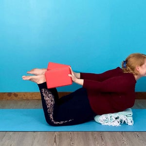 A person demonstrates supported Dhanurasana (Bow Pose) using blocks to press into the ankles