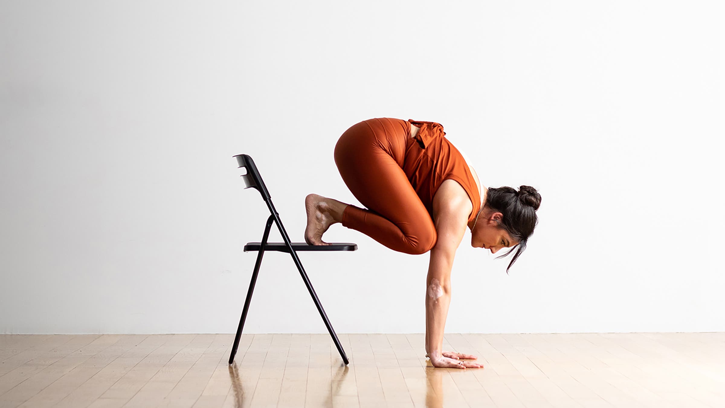 Woman in a Crow Pose modification with a chair