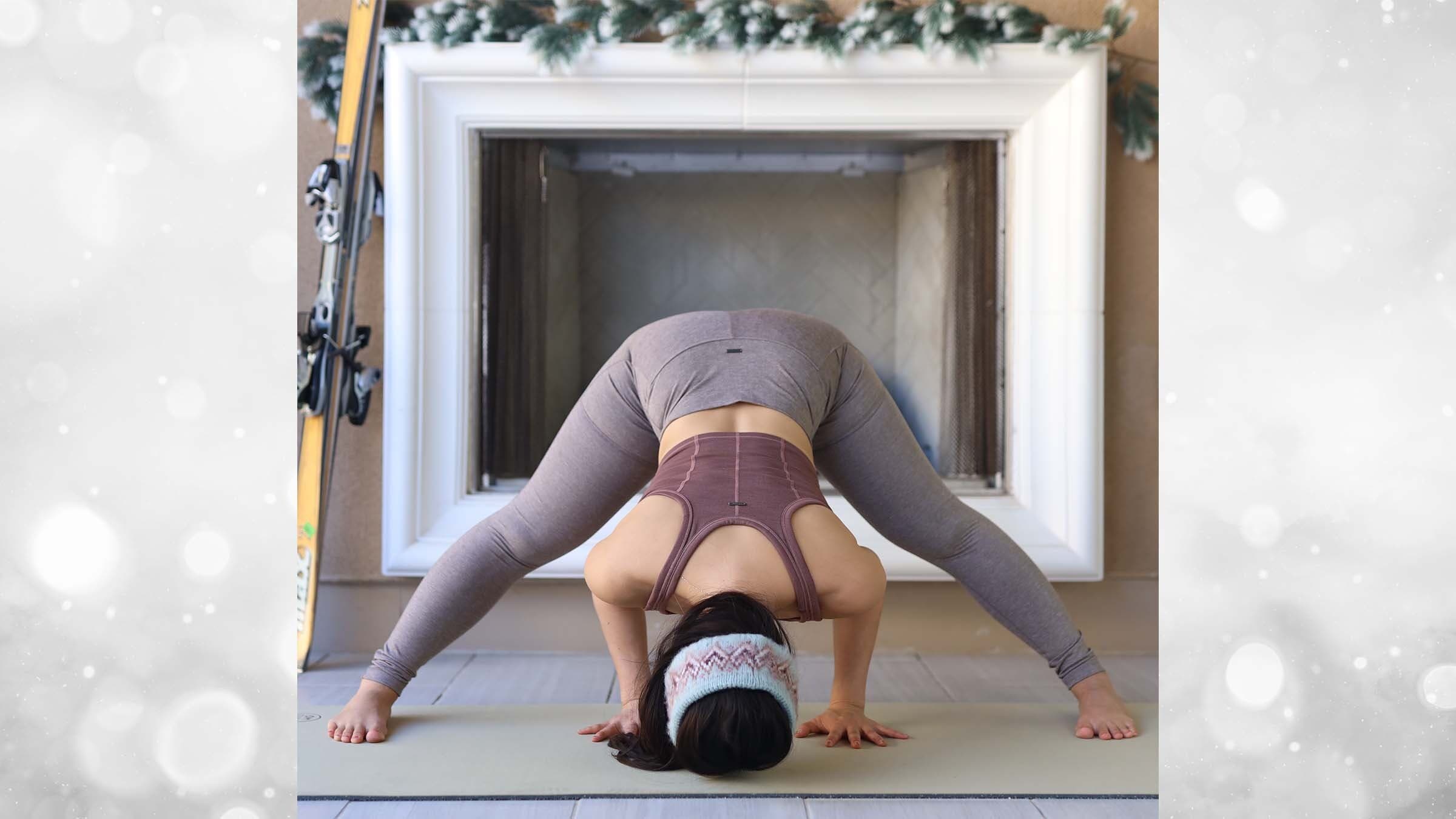 Ingrid Yang in wide leg forward fold in front of a fireplace