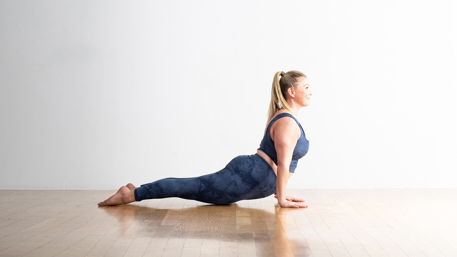 Blonde woman in blue tights and t-shirt practices Upward Facing Dog