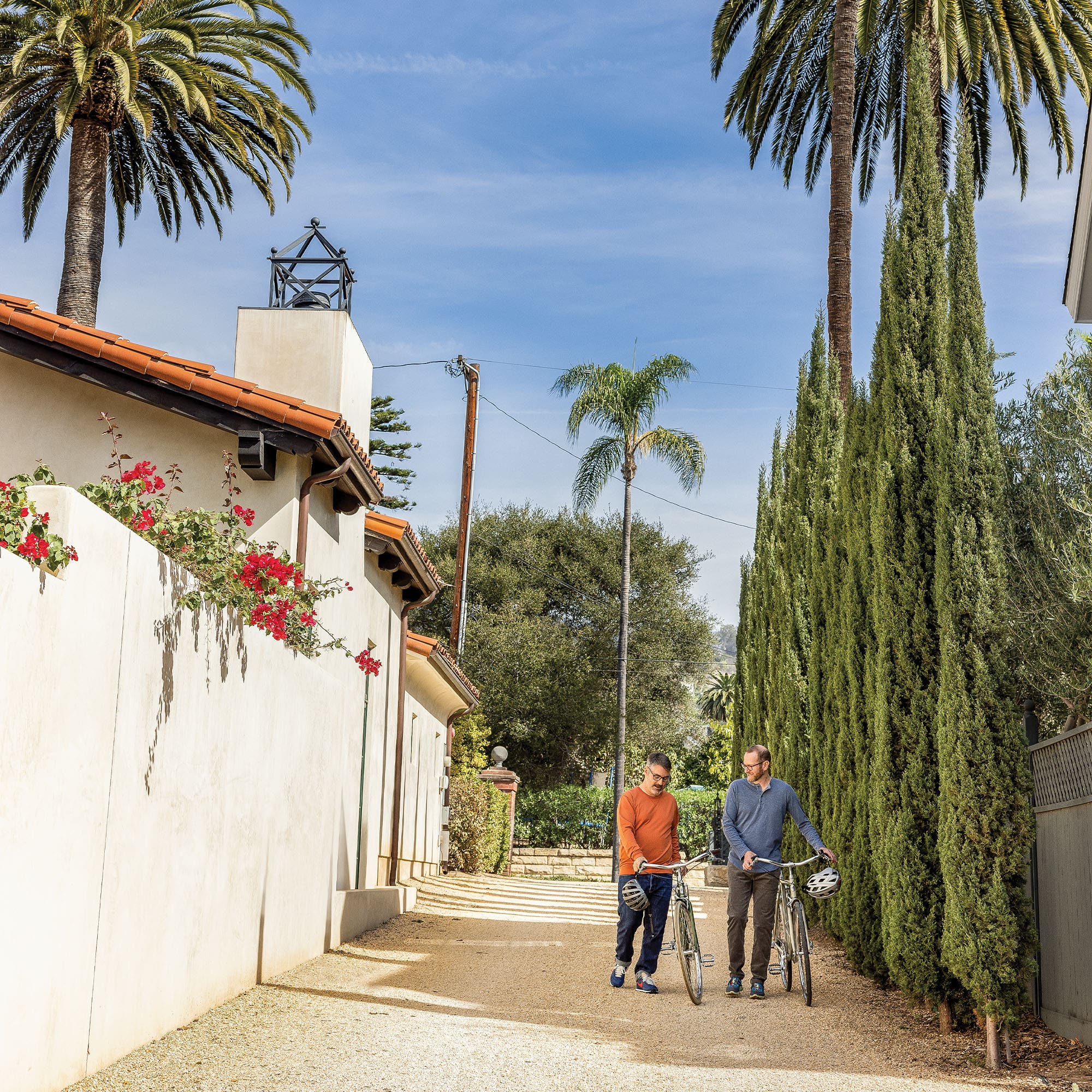 Heyman and Fratus walking down a tree-lined driveway with their bikes