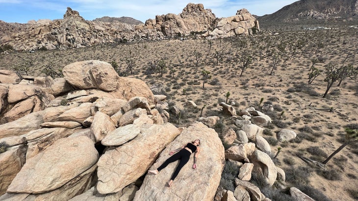 A person lies in Savasana (Corpse Pose) on a rock in the outdoors