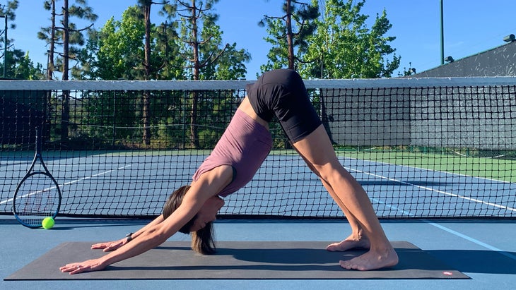 A person demonstrates Downward-Facing Dog on a tennis court