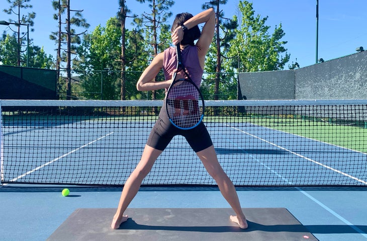 A person demonstrates the arms of Gomukhasana (Cow Face Pose) using a tennis racket