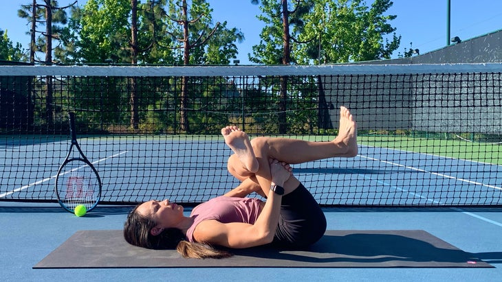 A person demonstrates supine Pigeon Pose in yoga on a tennis court