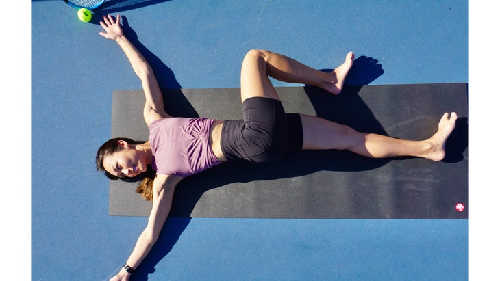 A person demonstrates a Supine Twist in yoga while lying on a tennis court